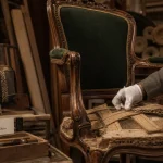 Rénovation fauteuil Voltaire en atelier, tapissier pose galon sur l’assise
